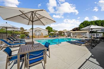 A poolside table and chairs are set up under a large umbrella.